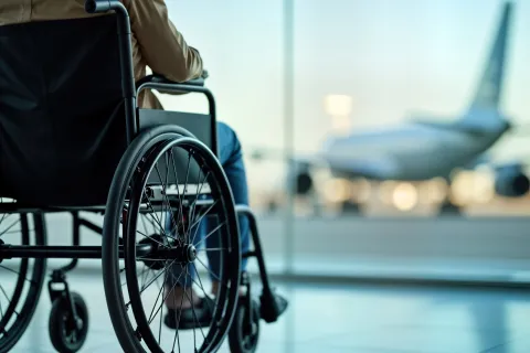 man sitting in wheelchair looking through window at airplane on the tarmac