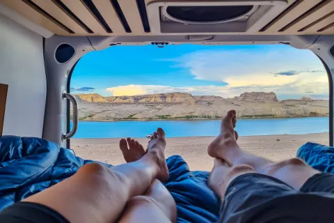 Legs of couple lying in camper van with panoramic sunset view of Wahweap Bay at Lake Powell, Glen Canyon