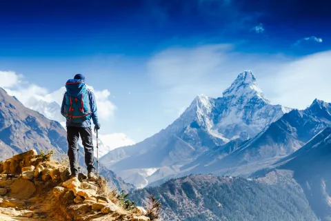 Hiker with trekking poles stands on the slope against the background of high snow-capped mountains