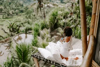 Young travel blogger and influencer girl relaxing in a bamboo house hotel in Bali surrounded by rice terraces and palm trees