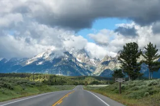 Scenic road approaching the Mount Moran Turnout with dramatic clouds surrounding the snowcapped Teton Range in Grand Teton National Park, Wyoming, USA