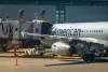 Calgary, Alberta, Canada. Nov 22, 2025. An American Airlines Airbus A320 is serviced by ground crew and jet bridge at a sunlit airport terminal gate.